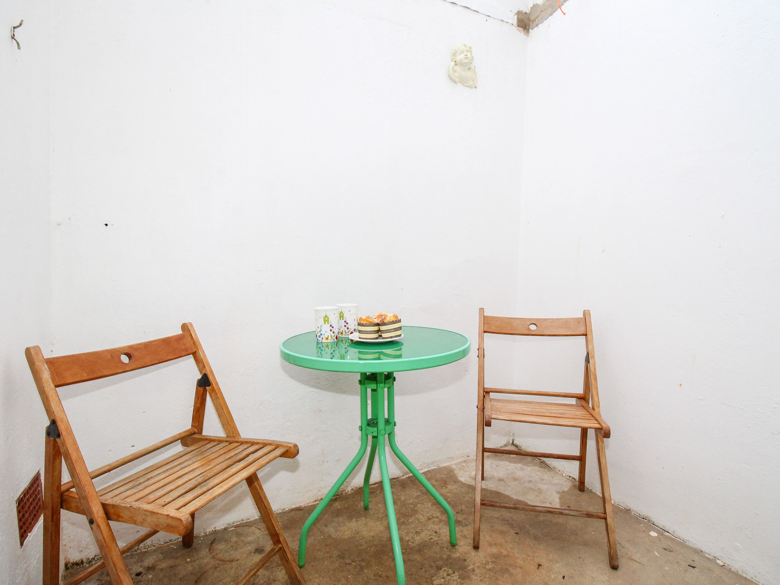 Une petite pièce avec deux chaises en bois et une table verte sur laquelle se trouvent un petit gâteau et deux tasses.