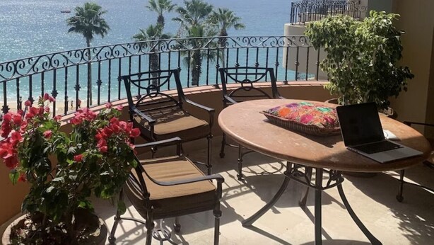 Un balcon avec vue sur la mer, comprenant une table ronde avec des chaises, un ordinateur portable et des plantes en pot.