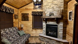 A cozy log cabin interior with a fireplace, wooden walls, and a patterned sofa.