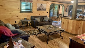 A cozy cabin interior with a wooden interior, a leather sofa, a coffee table, and a dining area.