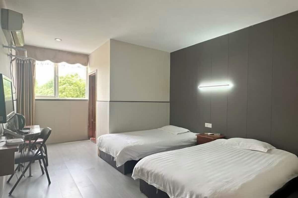 A hotel room with two beds, a desk with a chair, a TV, and a window with curtains.