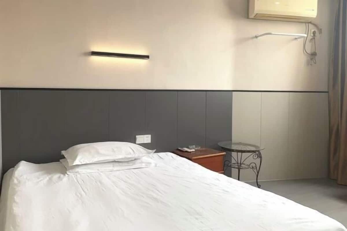 A hotel room with a bed, a small table, and a wall-mounted light fixture.