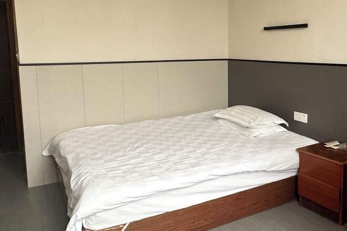 A single bed with a wooden frame, a bedside table with a phone, and a wall-mounted light switch.