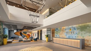 A modern hotel lobby with a reception desk, seating area, and a staircase. - HIIVE by fusion Binh Duong - VSIP 1 (Ho Chi Minh City)