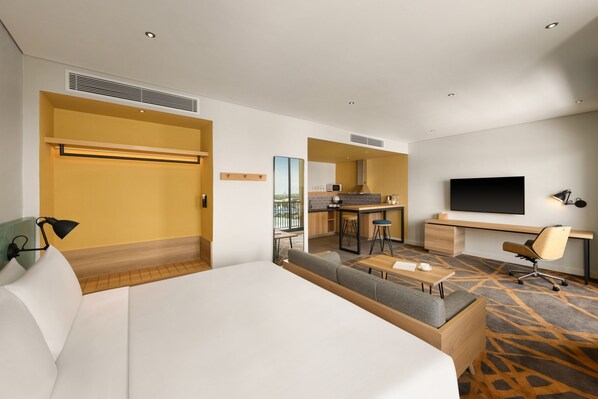 Una habitación de hotel con una cama grande, un escritorio, un sofá, un televisor y una kitchenette.