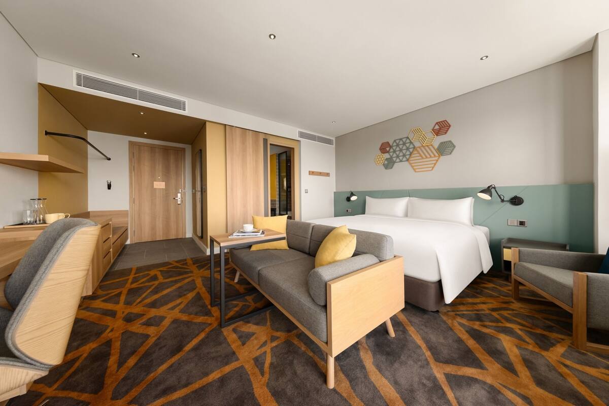A modern hotel room with a sofa, a bed, a desk, and a chair.