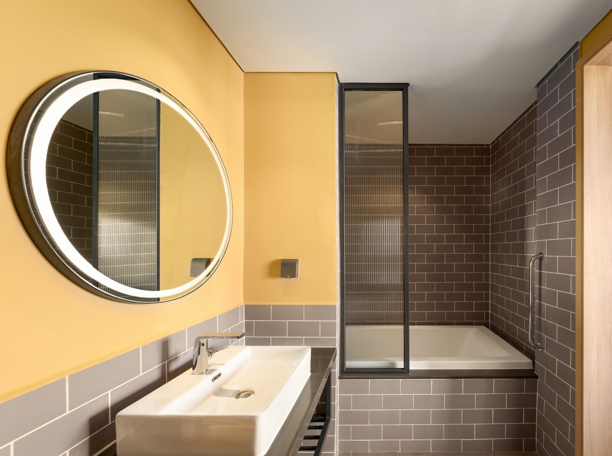 A modern bathroom with a rectangular sink, a round mirror, and a glass-enclosed shower.