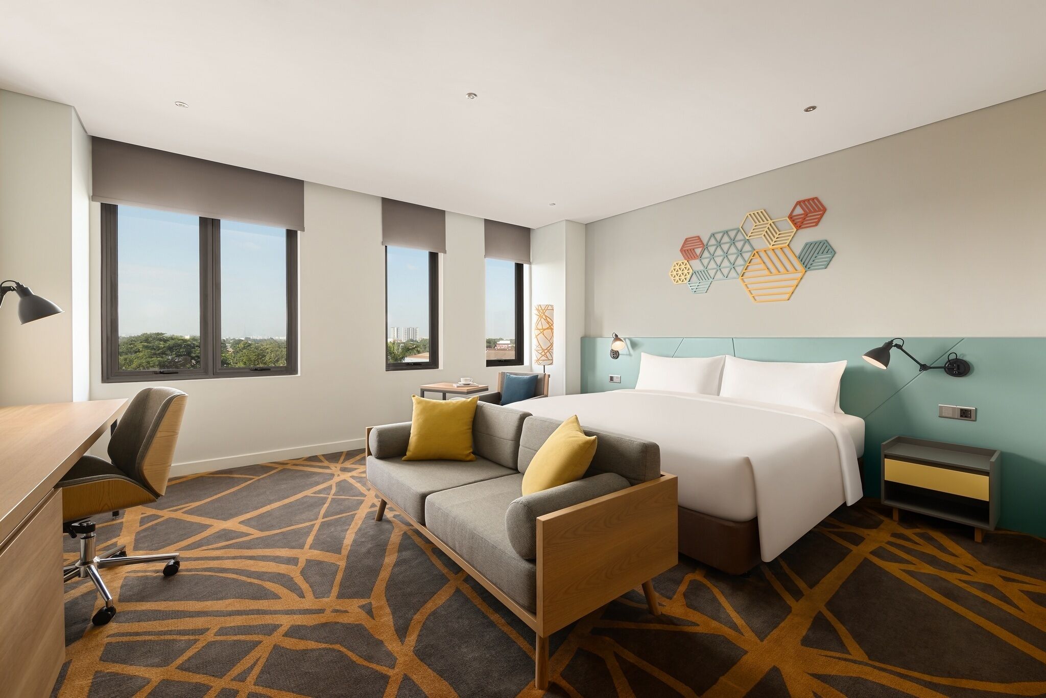 Une chambre d’hôtel moderne équipée d’un lit, d’un canapé, d’un bureau et de grandes fenêtres.