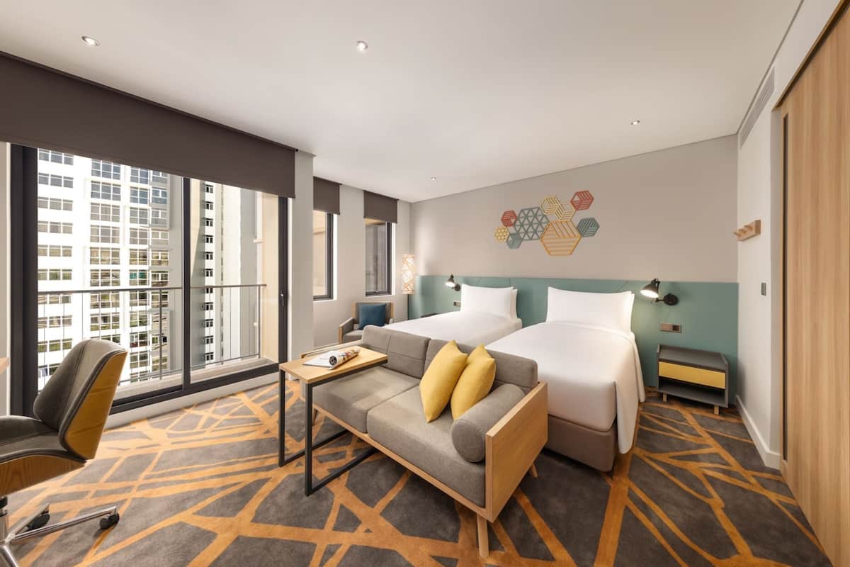 A hotel room with two beds, a sofa, a desk, and a chair.
