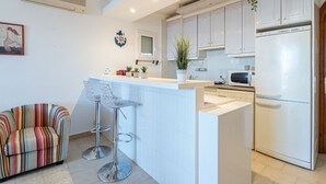 A modern kitchen with white cabinets, a stainless steel refrigerator, and a bar area with two bar stools.