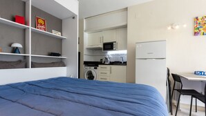 Une chambre à coucher de taille réduite, dotée d’un grand lit, d’une petite kitchenette et d’un bureau avec une chaise.