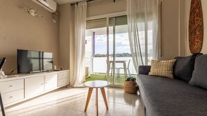 Un salon moderne doté d’un téléviseur à écran plat, d’un canapé gris et d’un balcon offrant une vue sur l’eau.