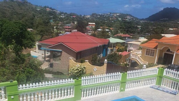 A swimming pool with a white fence and a view of houses and hills in the background. - Corinth Convinced Apartment One (Gros Islet)
