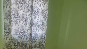 A small, single-bed room with a floral-patterned curtain and a plain white bedspread. - Corinth Convinced Apartment One (Gros Islet)