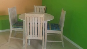A dining area with a round table and four chairs, each with a plaid cushion. The walls are painted in two colors: orange and green. - Corinth Convinced Apartment One (Gros Islet)