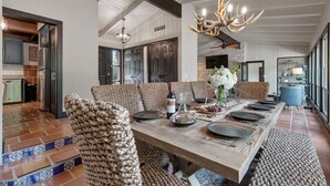 Un comedor espacioso con una larga mesa de madera, sillas estampadas y una original lámpara de astas.