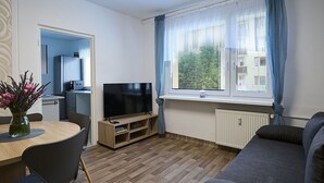 A modern living room with a flat-screen TV, a dining table with chairs, a sofa, and a window with curtains. - Lovely apartment for 6 guests with WIFI, TV and balcony (Jilemnice)