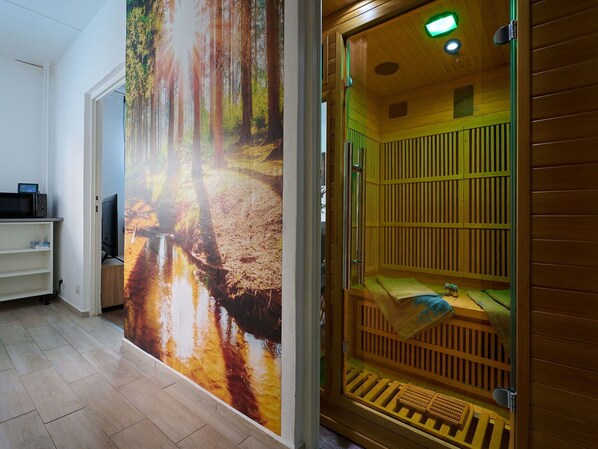 A room with a large forest mural, a sauna, and a television on a shelf.