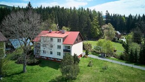 A two-story building with a red roof, surrounded by a green landscape and trees. - Nice apartment for 4 guests with WIFI, TV, balcony and pets allowed (Jilemnice)