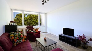 A modern living room with a red sofa, a black coffee table, a red armchair, a black TV stand, and a large window with a view of trees. - Nice apartment for 4 guests with WIFI, TV, balcony and pets allowed (Jilemnice)