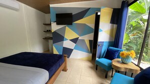 Une pièce comprenant un lit, une chaise, une petite table avec un vase de fleurs et un téléviseur fixé au mur.