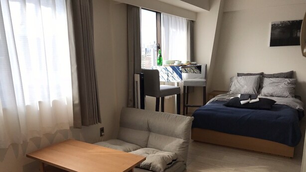 A modern, well-lit bedroom with a bed, a sofa, a wooden table, and a desk with a chair. - Shinosaka 1 min  (Osaka)