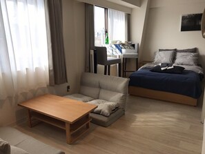 Un dormitorio moderno y bien iluminado, con cama, sofá, mesa de madera y escritorio con silla.