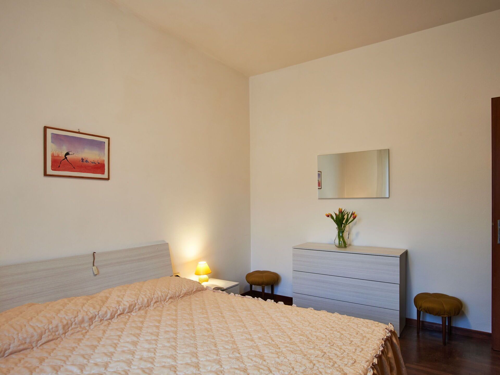 A bedroom with a bed, a nightstand, a dresser, a mirror, and a painting on the wall.