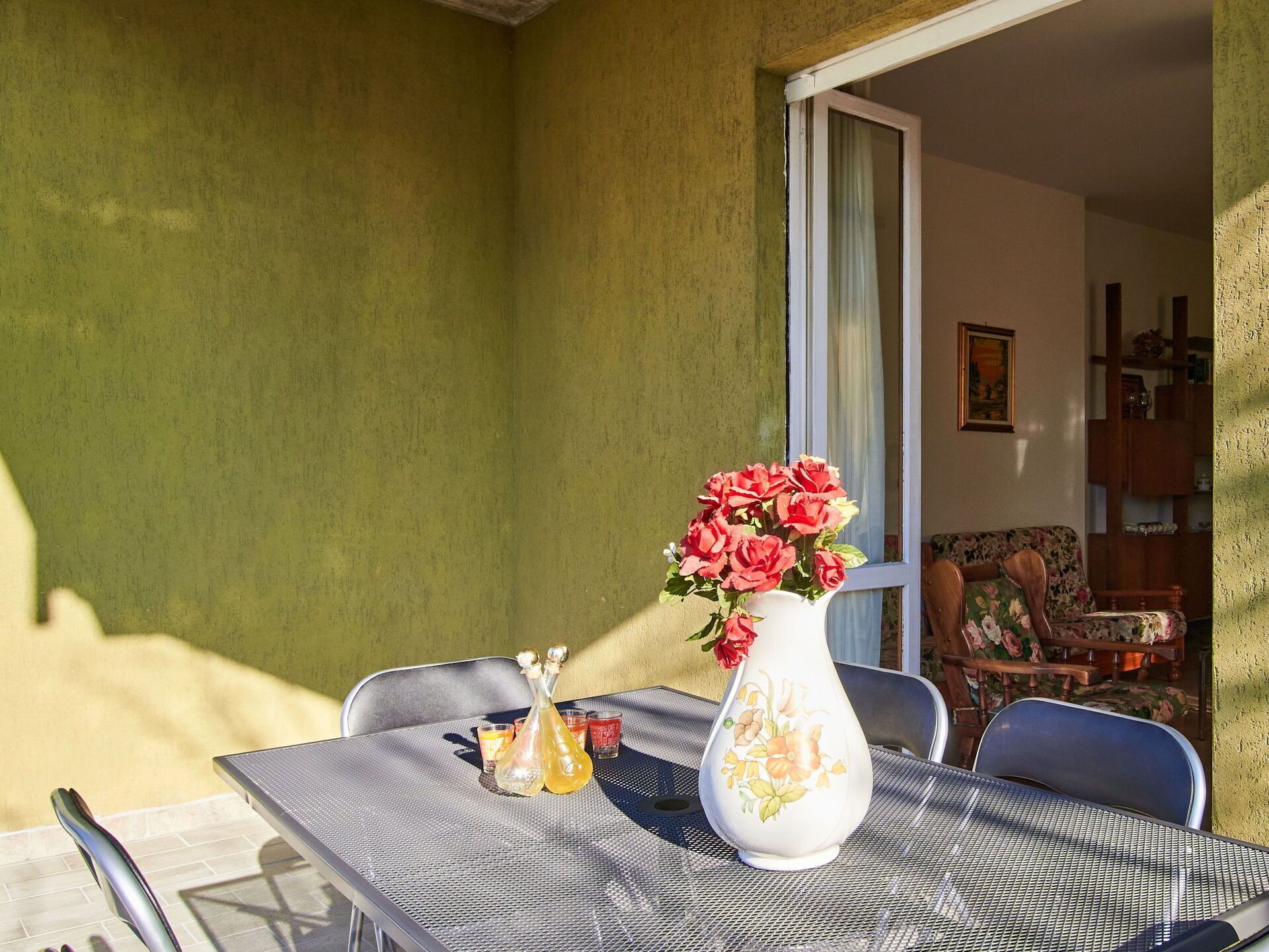 A patio with a table, chairs, a vase with flowers, and a dining area visible through an open door.