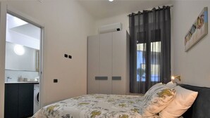 A bedroom with a bed, a wardrobe, a washing machine, and a bathroom with a mirror.
