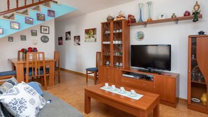 A living room with a sofa, coffee table, TV, wooden cabinets, and a staircase. - Beautiful private villa for 6 guests with private pool, TV and patio (Miami Platja)