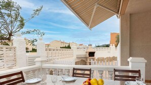 A dining area with a table set for four, a bowl of fruit, and a view of the surrounding buildings. - Beautiful private villa for 6 guests with private pool, TV and patio (Miami Platja)