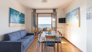 Ein gemütliches Wohnzimmer mit einer Couch, einem Esstisch mit Stühlen und Meerblick durch eine Glastür.