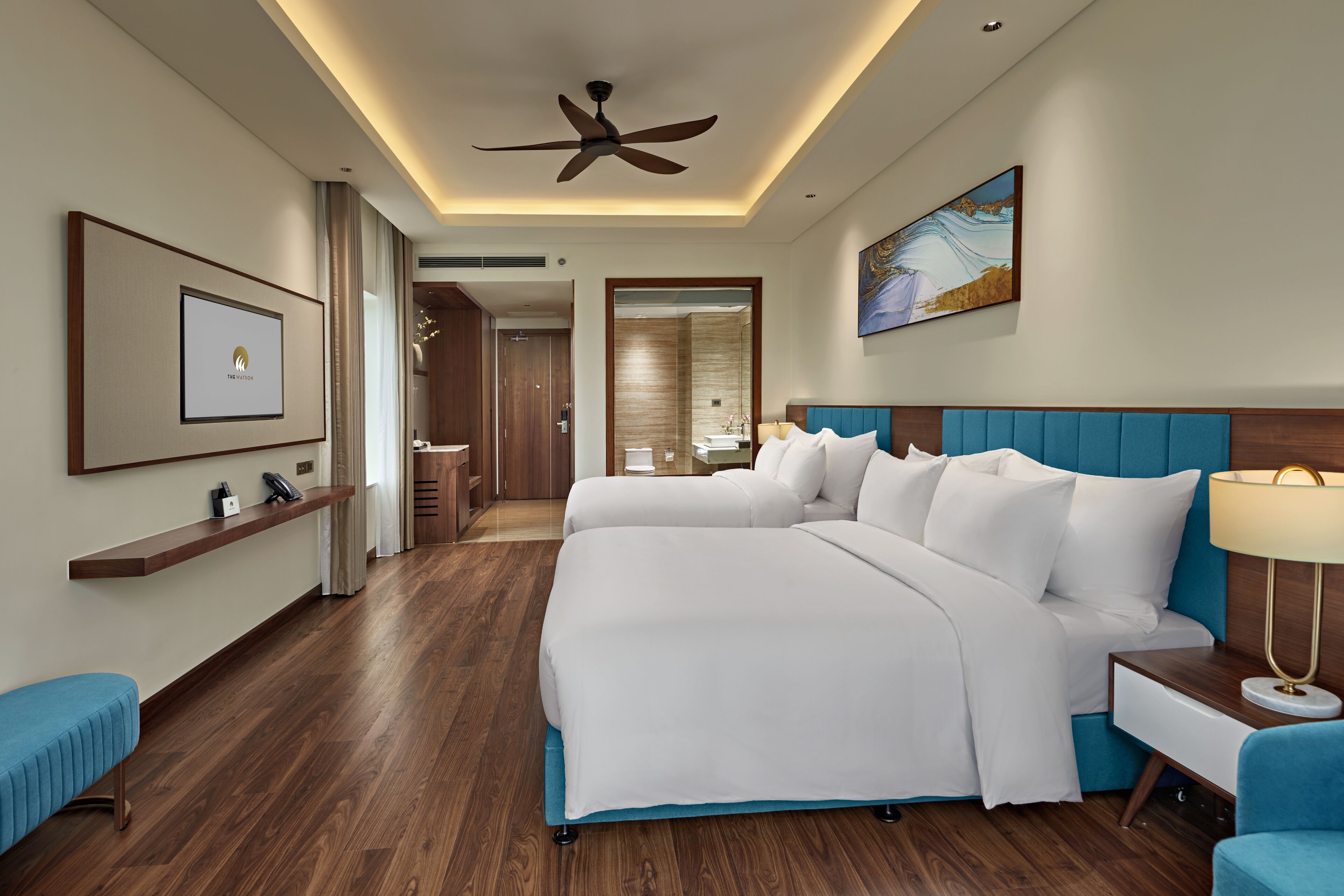 A hotel room with a large bed, a desk, a chair, a ceiling fan, and a painting on the wall.