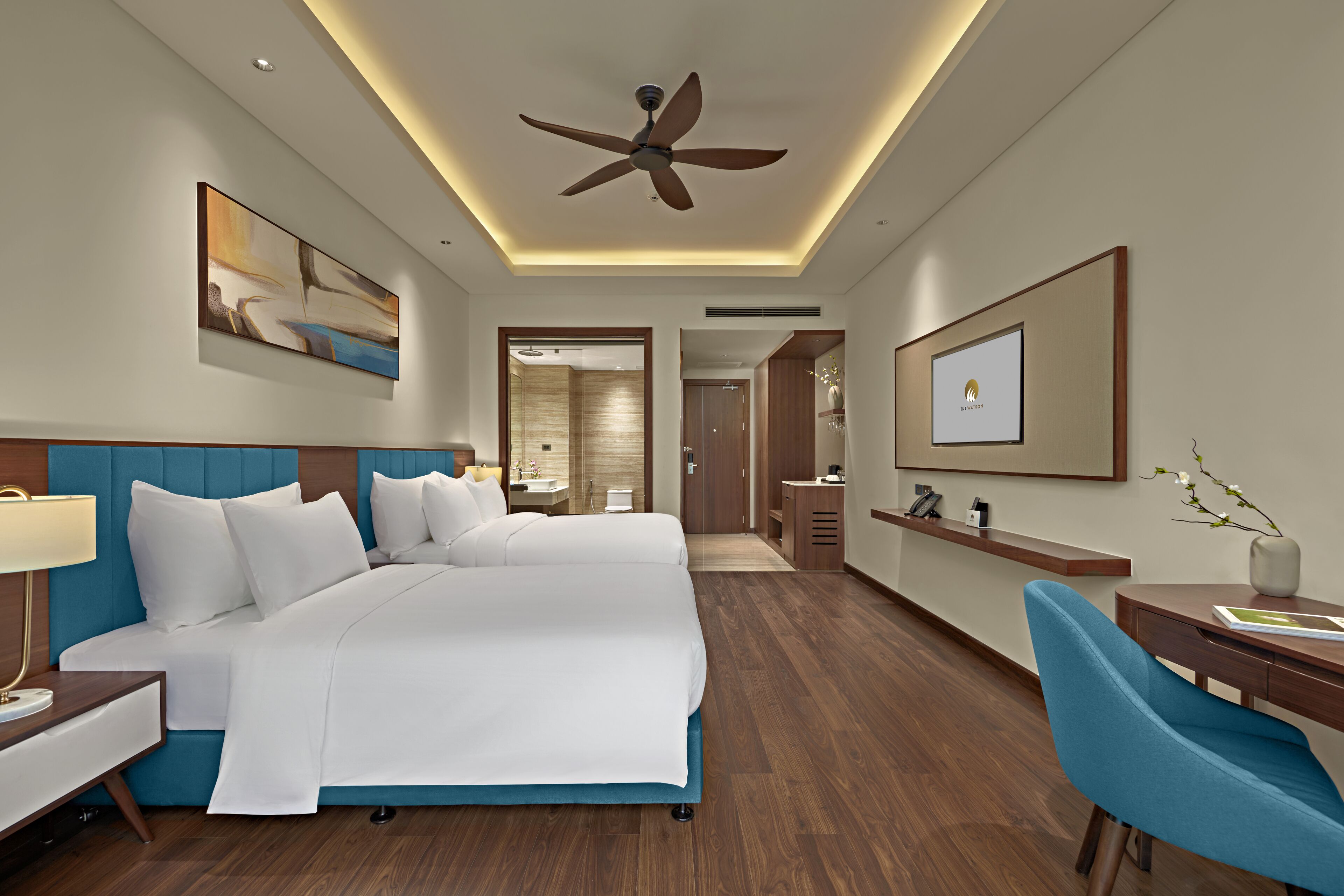 Une chambre d’hôtel avec un grand lit, un bureau, une chaise, un ventilateur de plafond et des œuvres d’art accrochées aux murs.