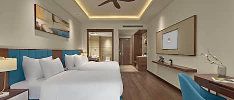 Une chambre d’hôtel avec un grand lit, un bureau, une chaise, un ventilateur de plafond et des œuvres d’art accrochées aux murs.