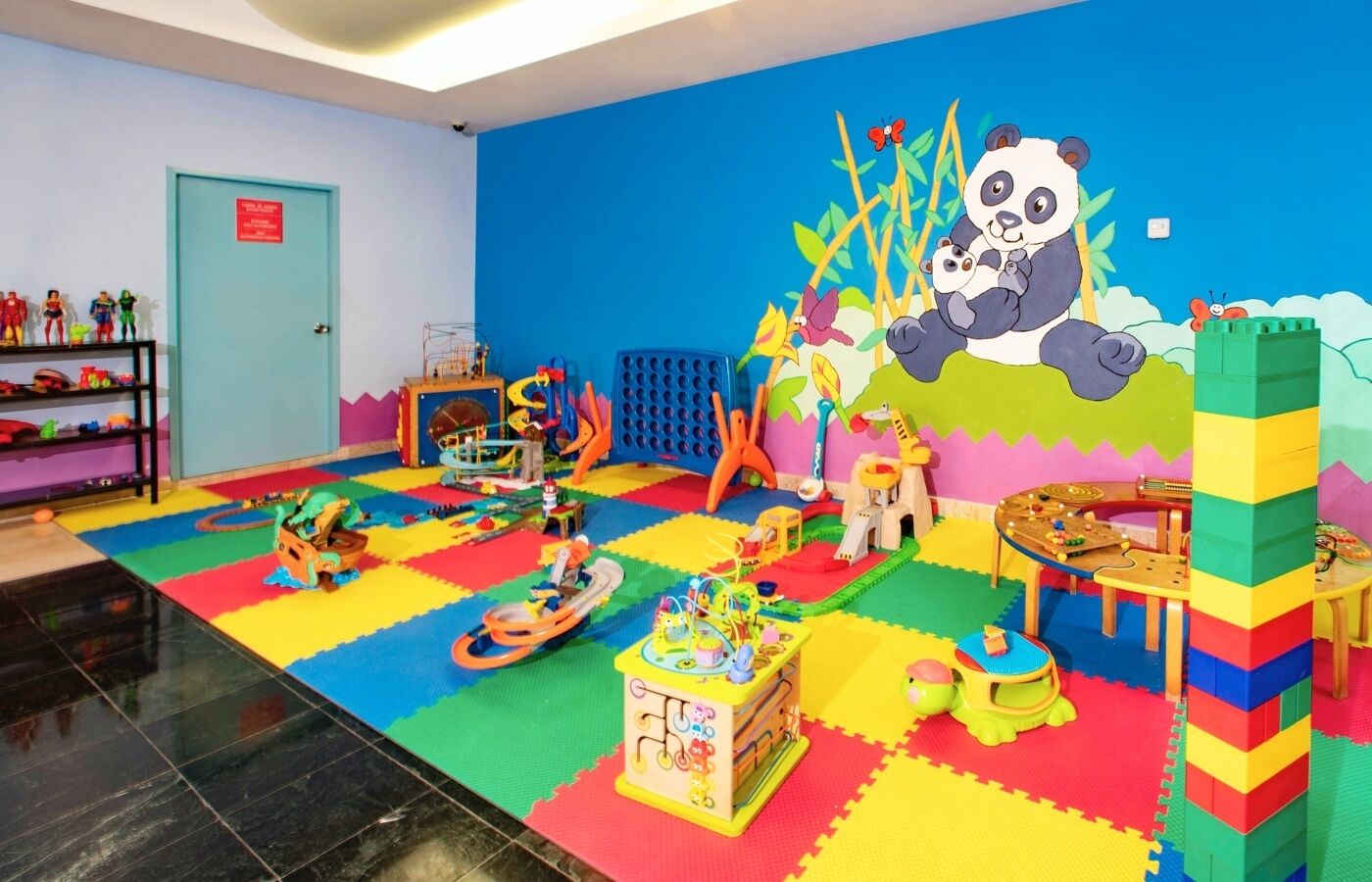 Un espace de jeux pour enfants avec des tapis en mousse colorés, des structures de jeu et une fresque représentant un panda sur le mur.
