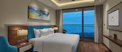 Quarto de hotel com uma cama grande, ventilador de teto, um quadro e vista para o mar.