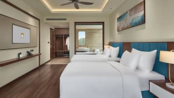 A hotel room with two beds, a ceiling fan, a large mirror, a painting, and a desk with a lamp.