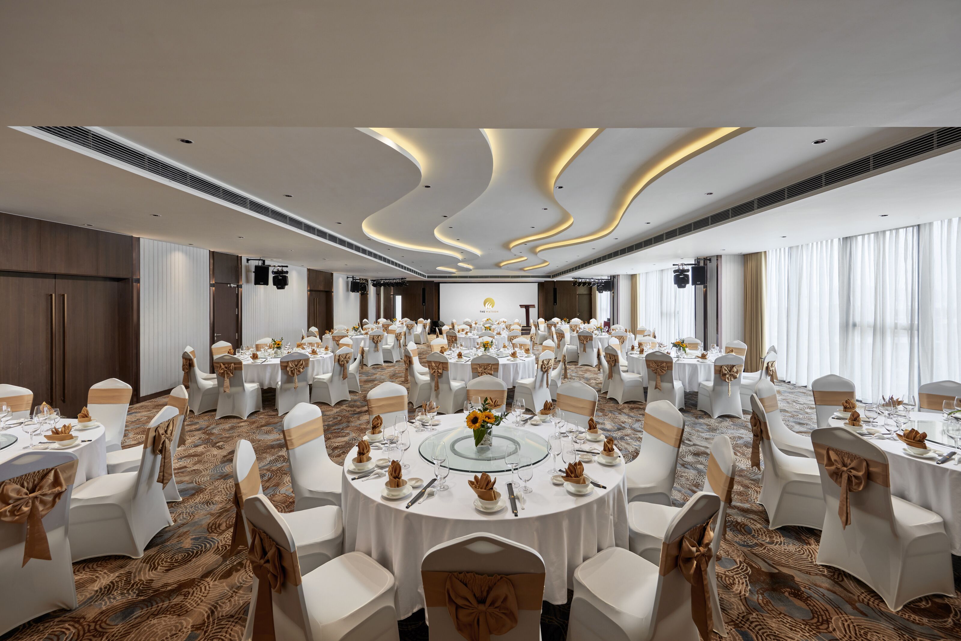 A large banquet hall with round tables, white chairs, and gold sashes.