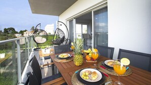 A balcony with a table set for breakfast, including plates of food, a pineapple, and a glass of orange juice. - Nice apartment for 4 people with A/C, WIFI, pool, TV and balcony (Portimão)