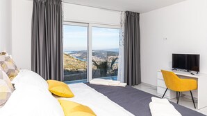 A modern hotel room with a large bed, a desk with a TV, and a scenic view through the window.
