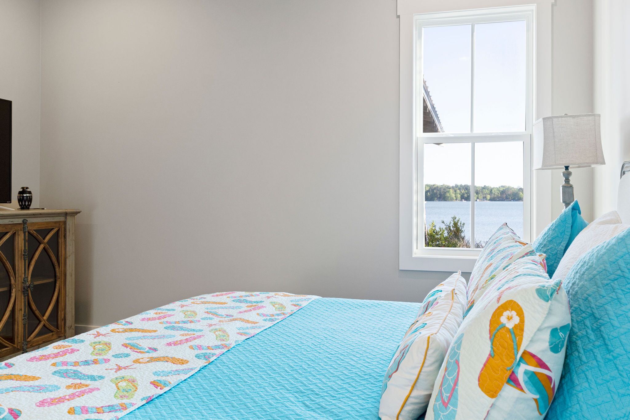 A bedroom with a bed, a window with a view of a body of water, and a wooden cabinet.