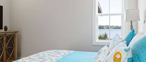 A bedroom with a bed, a window with a view of a body of water, and a wooden cabinet.