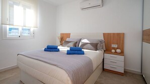 A modern bedroom with a bed, a nightstand, a wall-mounted air conditioner, and a window with blinds. - Beautiful apartment for 4 guests with pool, A/C, WIFI, TV and balcony (Calafell)