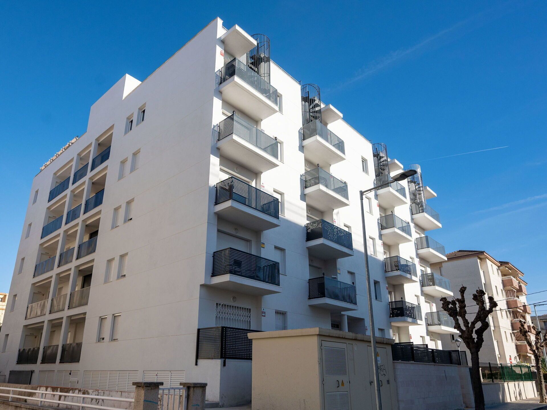 A multi-story residential building with balconies, a gated entrance, and a clear blue sky.