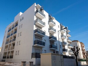 Un edificio residencial de varios pisos con balcones, un acceso mediante portón y un cielo azul despejado.