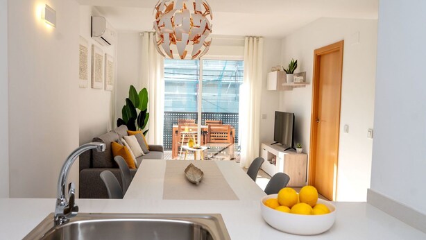A modern kitchen with a stainless steel sink, a dining area with a white table, and a living space with a sofa and a TV. - Beautiful apartment for 4 guests with pool, A/C, WIFI, TV and balcony (Calafell)