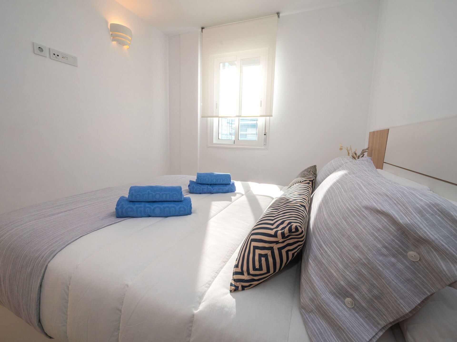 Un lit bien fait, avec des serviettes bleues, un coussin à motifs et une couverture rayée.