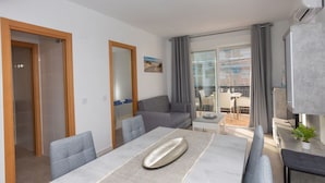 Una sala de estar moderna con una mesa de comedor, sofá gris y un balcón con vistas.